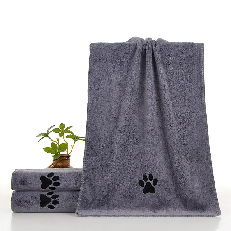 A dark gray pet bath towel with a paw print design is displayed next to a small potted plant.