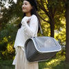 A woman is holding a gray breathable pet carrier bag for cats and small dogs outdoors.