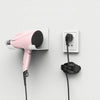 A pink hair dryer is mounted on a wall, with its cord neatly organized by a silicone cable organizer.
