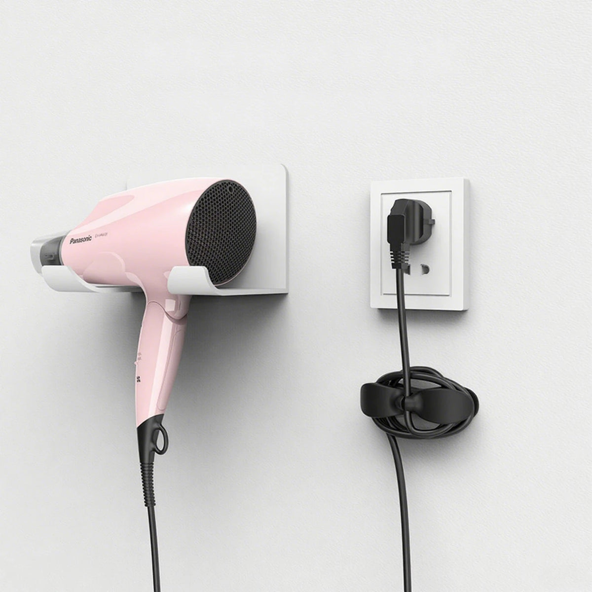 A pink hair dryer is mounted on a wall, with its cord neatly organized by a silicone cable organizer.