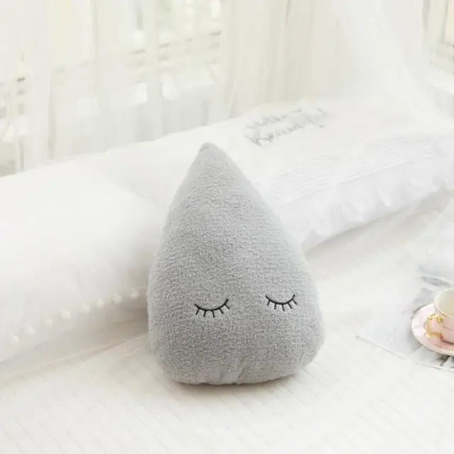 A soft gray plush pillow shaped like a cloud with closed eyes resting on white bedding.