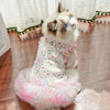 A fluffy white and gray cat wearing a floral pink ruffled vest.