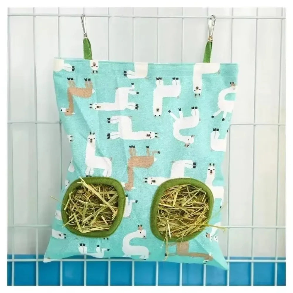 A light blue fabric bag with white silhouette drawings of unicorns and a green straw hay feeder inside, hanging on a wire gri