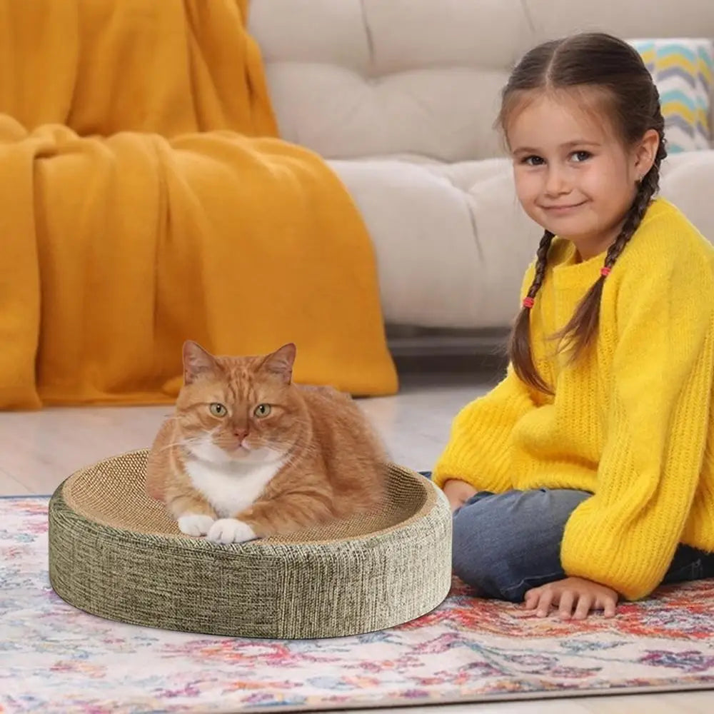 Una niña está sentada en una alfombra colorida junto a una plancha ovalada de sisal para arañazos y cama.