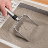 A hand is using a stainless steel cat litter scoop to move granular litter inside a white plastic container.