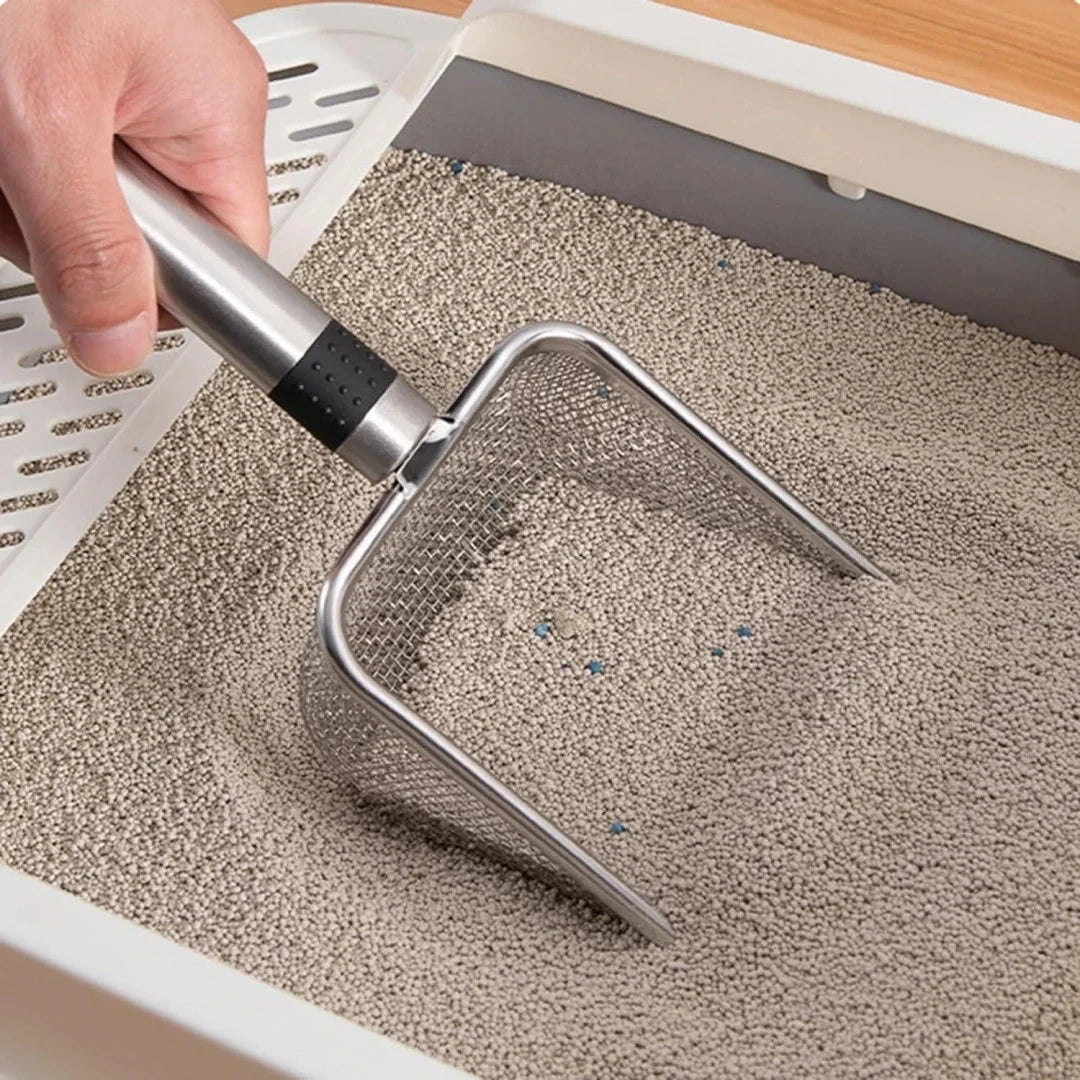 A hand is using a stainless steel cat litter scoop to move granular litter inside a white plastic container.