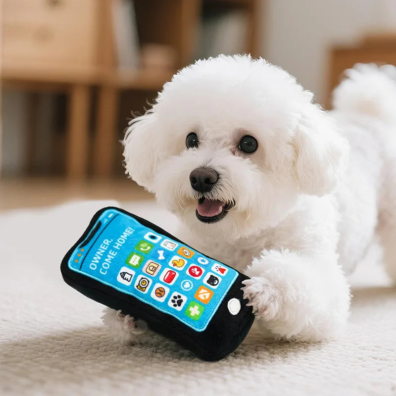 A white dog is lying next to a black phone-shaped squeaky toy with crinkle paper.