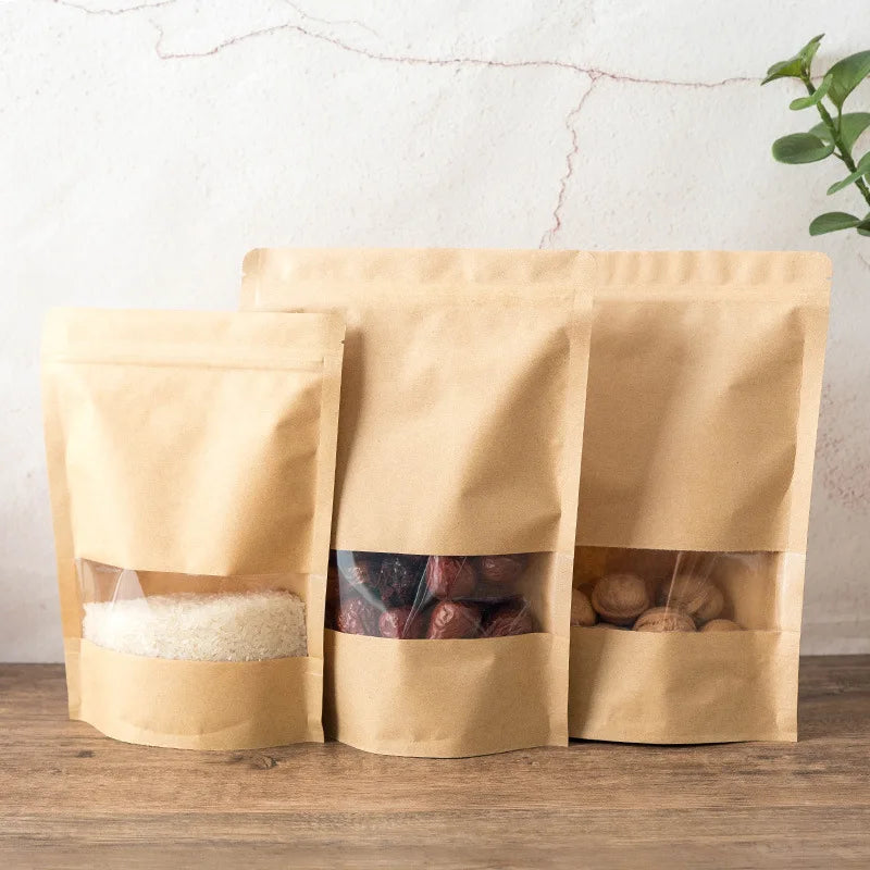 Drei kraftpapier-Zipertaschen gefüllt mit weißen Körnern, getrockneten Früchten und Nüssen auf einer Holzoberfläche.