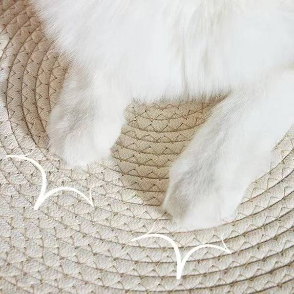 A fluffy white cat's paws resting on a beige handwoven rattan cat bed.