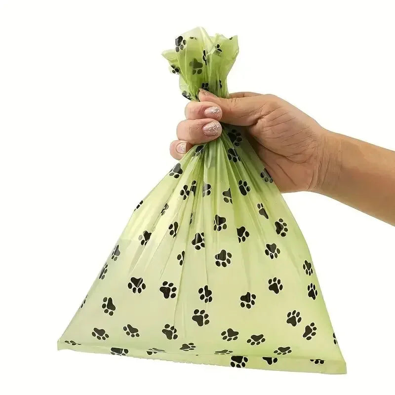 A hand is holding a clear plastic bag filled with black paw prints, representing heavy duty pet waste bags.