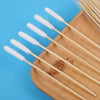 A set of wooden ear cleaning cotton swabs with white cotton tips arranged on a light blue background.