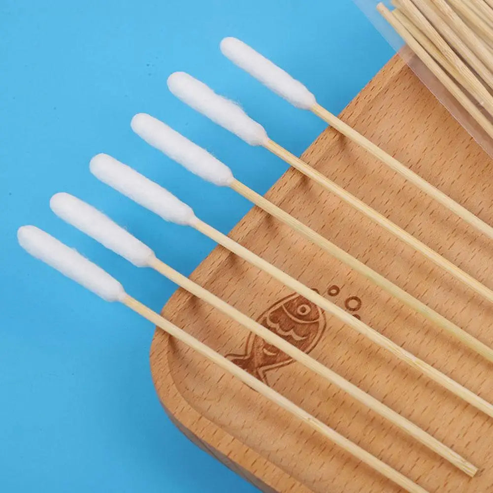 A set of wooden ear cleaning cotton swabs with white cotton tips arranged on a light blue background.