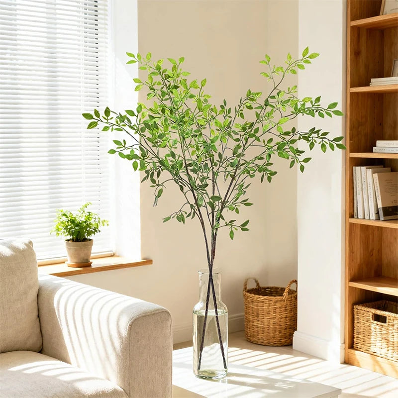 A tall glass vase filled with artificial bamboo stems used as a decorative filler in a bright living room setting.