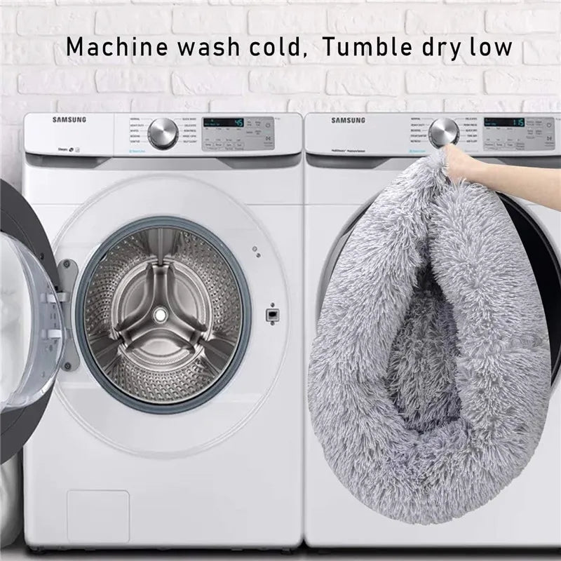 A close-up of a washing machine door showing a fluffy gray pet bed being placed inside.