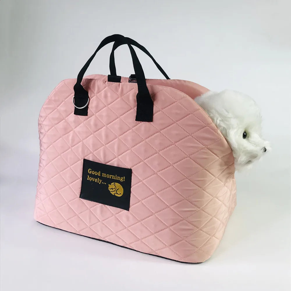 A pink quilted portable soft-sided pet carrier with black handles and a yellow graphic tag, next to a white dog.