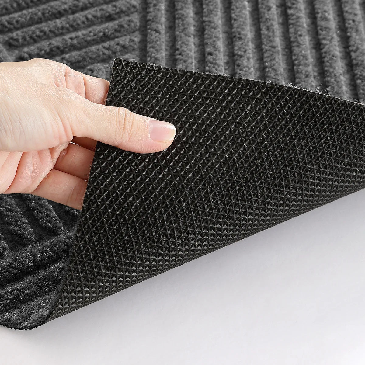 A hand is touching a black 3D geometric non-slip doormat with a textured surface.