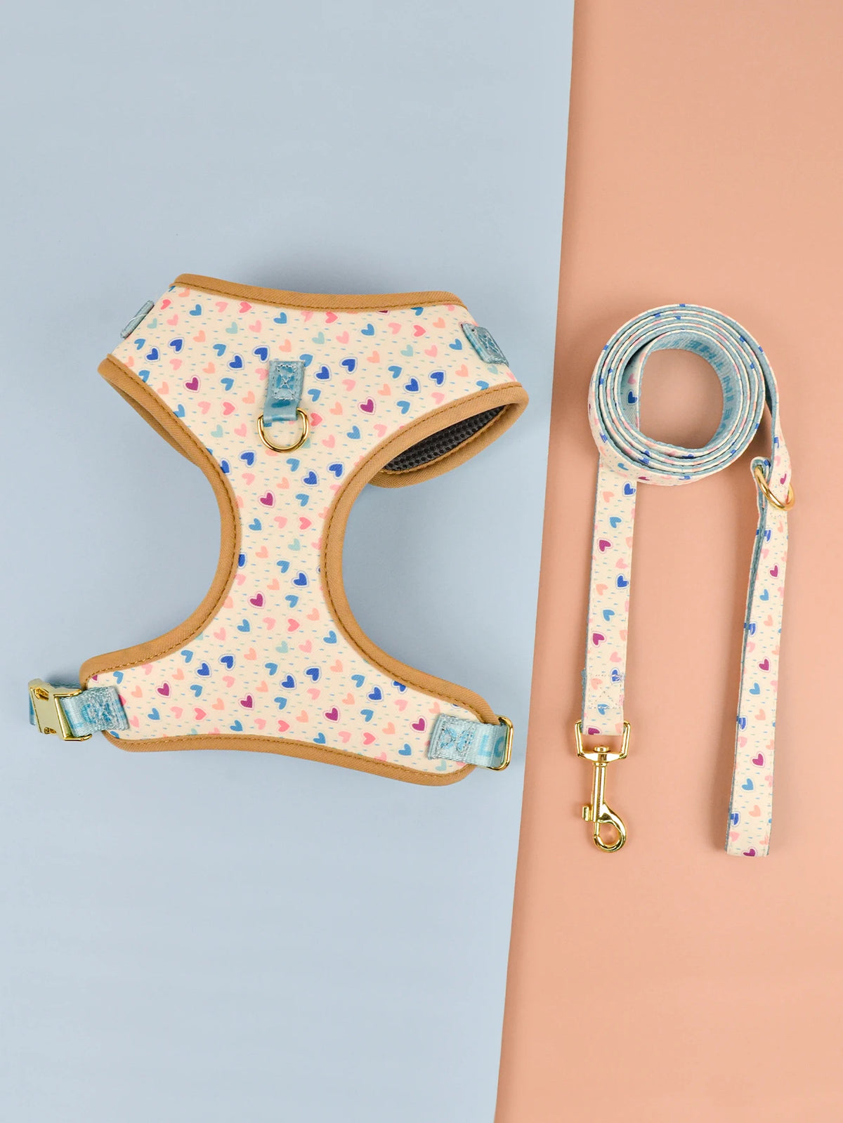 A light pink pet harness with a matching blue patterned leash displayed on a peach background.