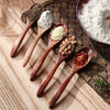 A set of six wooden spoons holding various spices and ingredients on a wooden board.