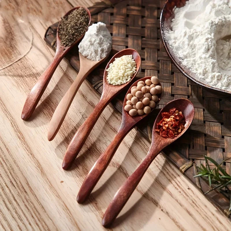 A set of six wooden spoons holding various spices and ingredients on a wooden board.