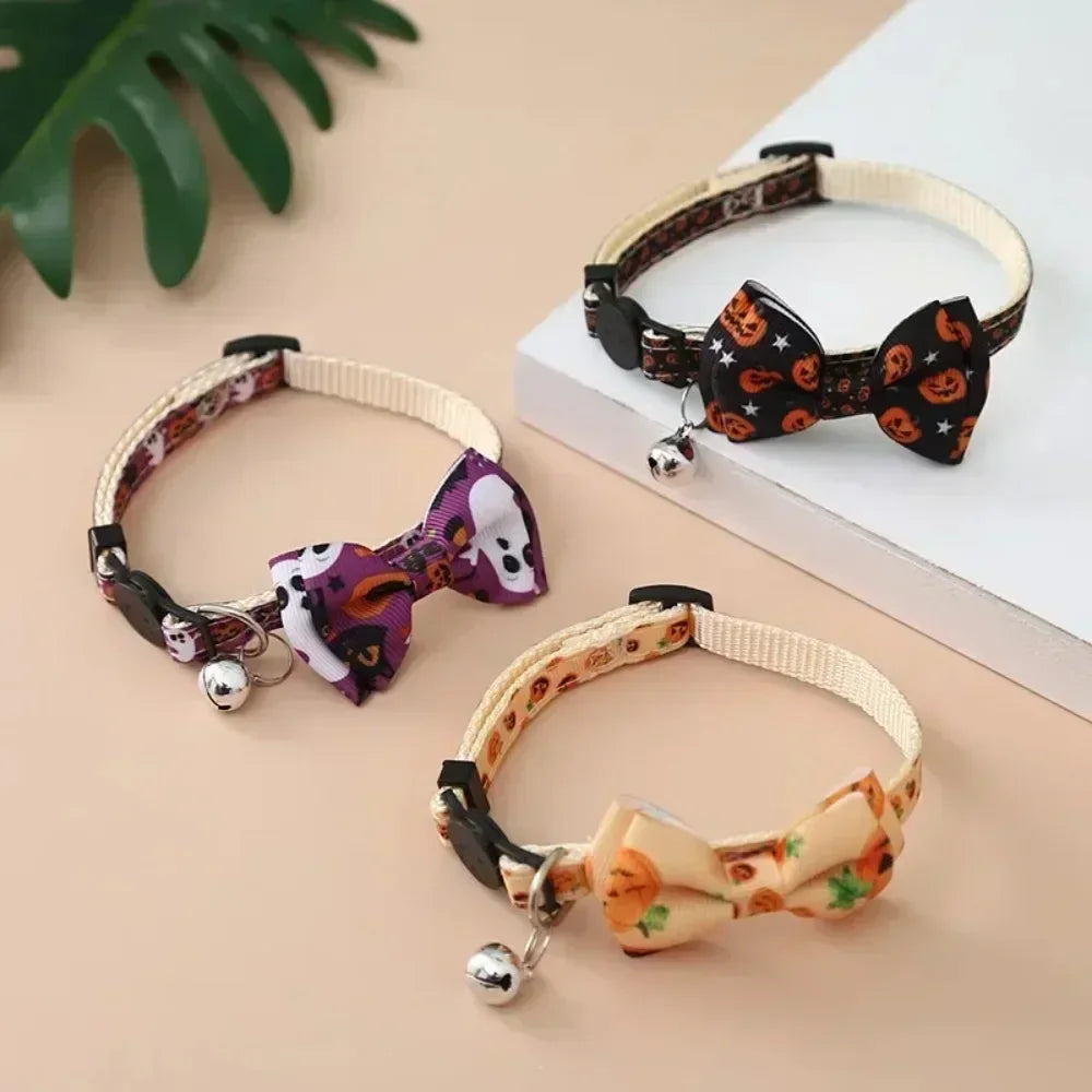 A black Halloween cat collar with a bow tie and bell, featuring a breakaway safety buckle, displayed on a white surface.