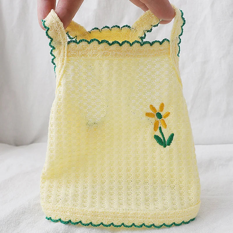 A yellow crocheted pet vest with green trim and a yellow floral embroidery on the front.