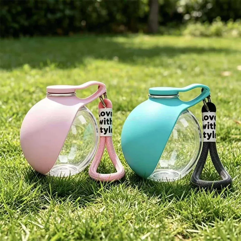 Two glass water dispensers with pink and teal lids and black straps resting on green grass.