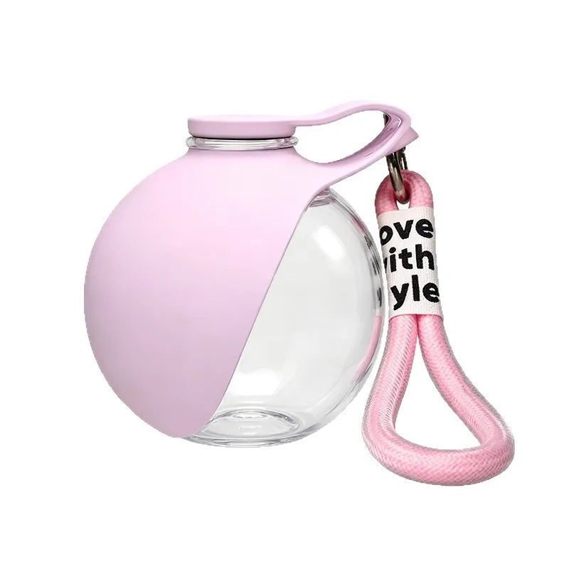 A pink glass water bottle with a lid and a pink braided strap attached, used for portable dog water.