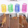 A set of colorful spring toys, including yellow, green, and blue rings, next to three cats playing with them.