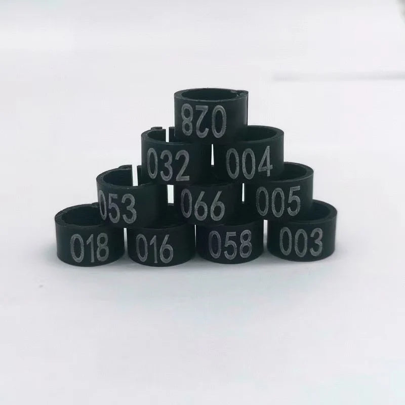 A collection of black plastic bird identification foot rings with various numerical markings stacked on a white surface.