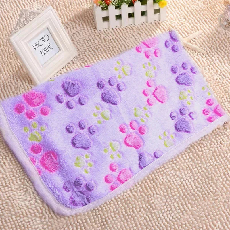 A purple flannel pet blanket featuring various colored paw print designs, resting on a beige textured surface.