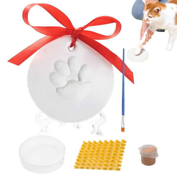 A pet paw print impression kit showing a white paw print, a paintbrush, and yellow impression pads.