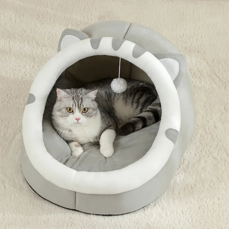 A domestic cat is relaxing inside a round, light gray pet bed designed to look like a cat cave.