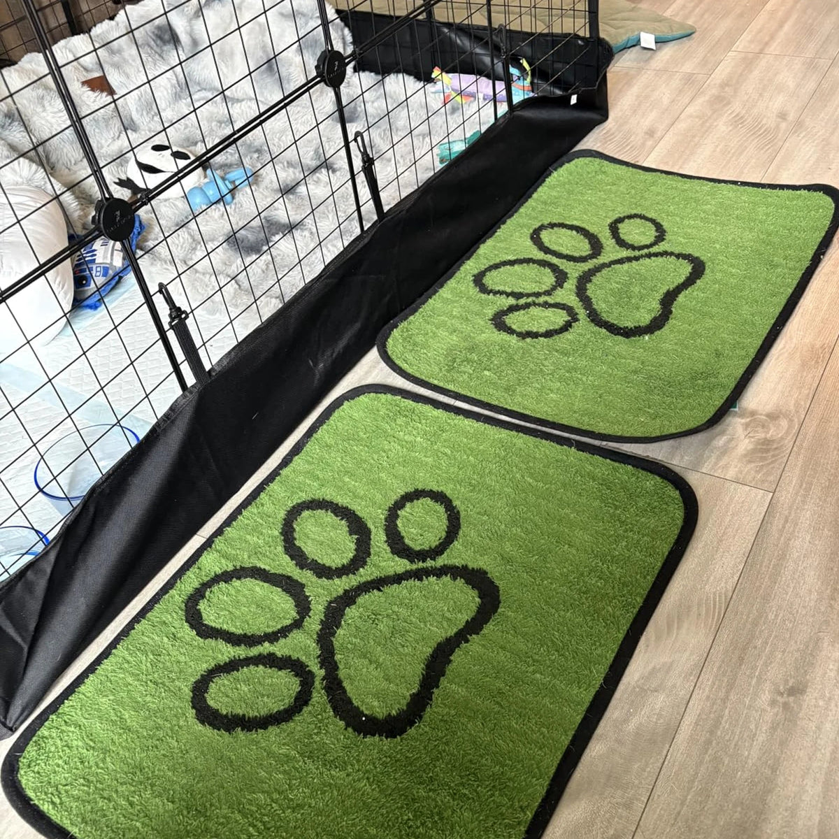 Two green dog urine training mats with paw prints are laid out on a light wood floor.