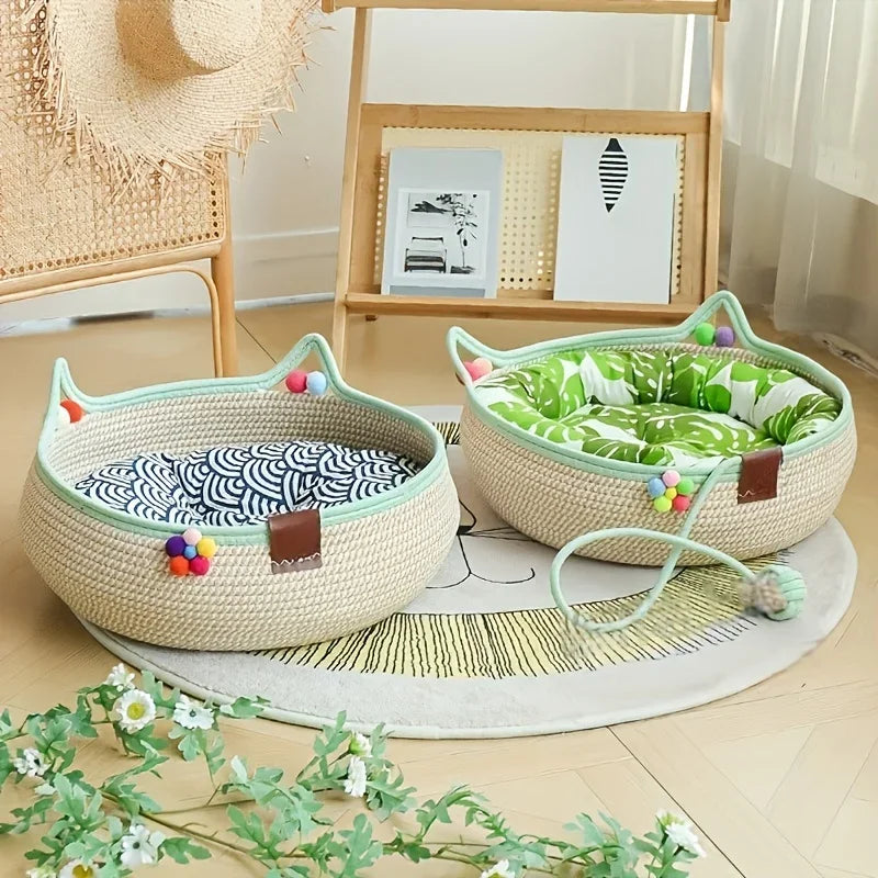 A beige woven cat scratcher and comfort bed with green and white fabric and colorful play balls on a light wood floor.