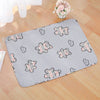 A gray pet cage mat with a pink and white plaid pattern is placed on a wooden floor.