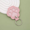 A pink leather paw print airtag keepsake with a silver ring attached, set against a light green background.
