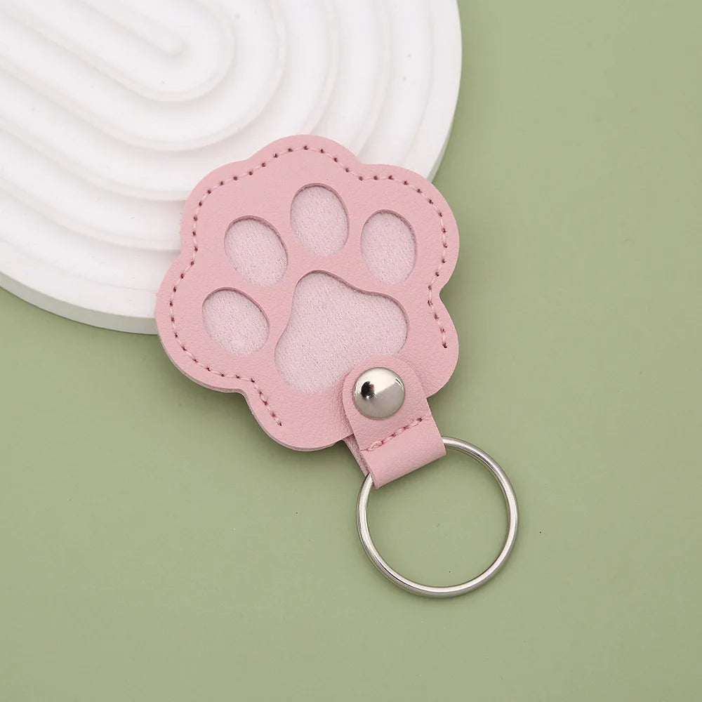 A pink leather paw print airtag keepsake with a silver ring attached, set against a light green background.