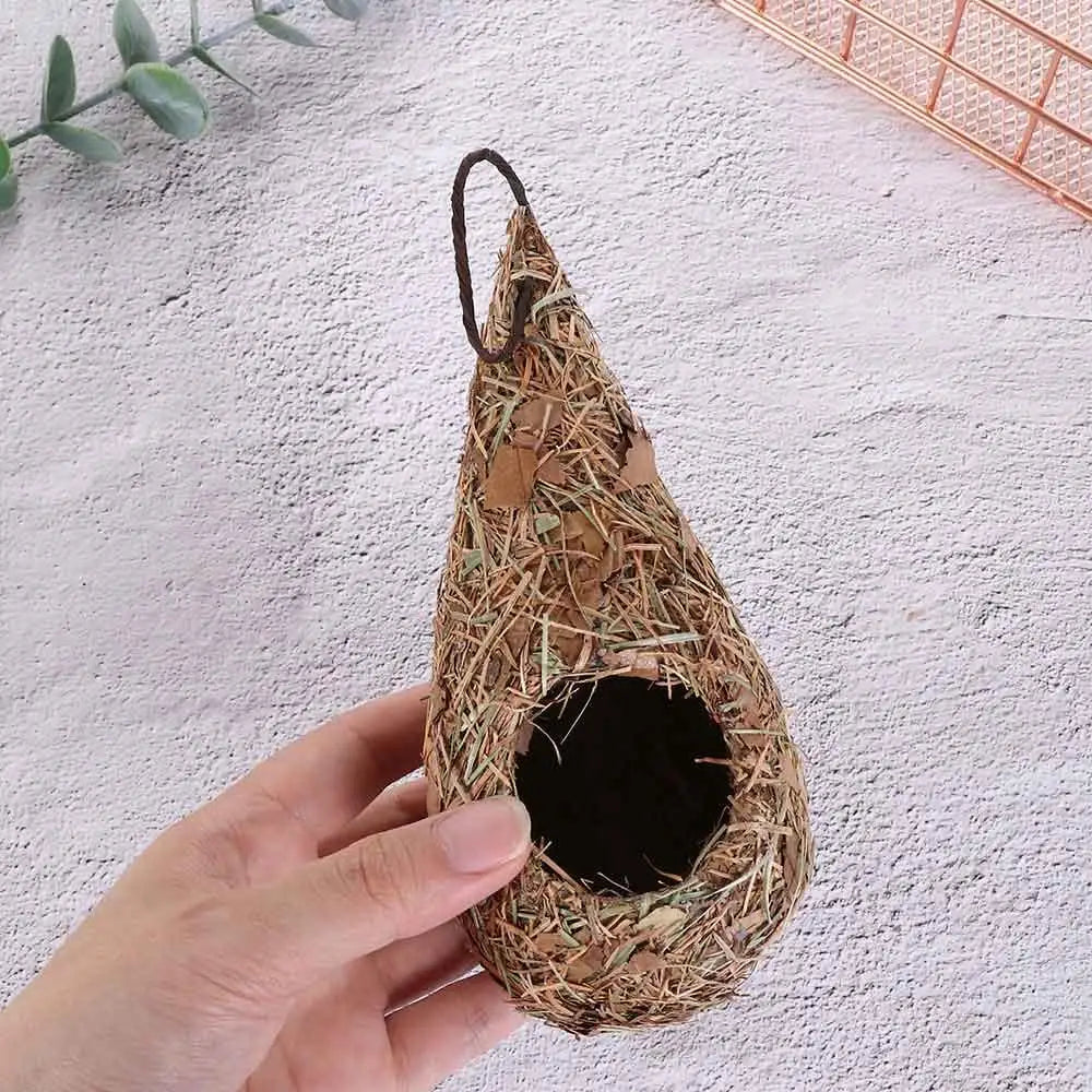 A hand-woven grass bird nest decoration is held in a person's hand against a light background.