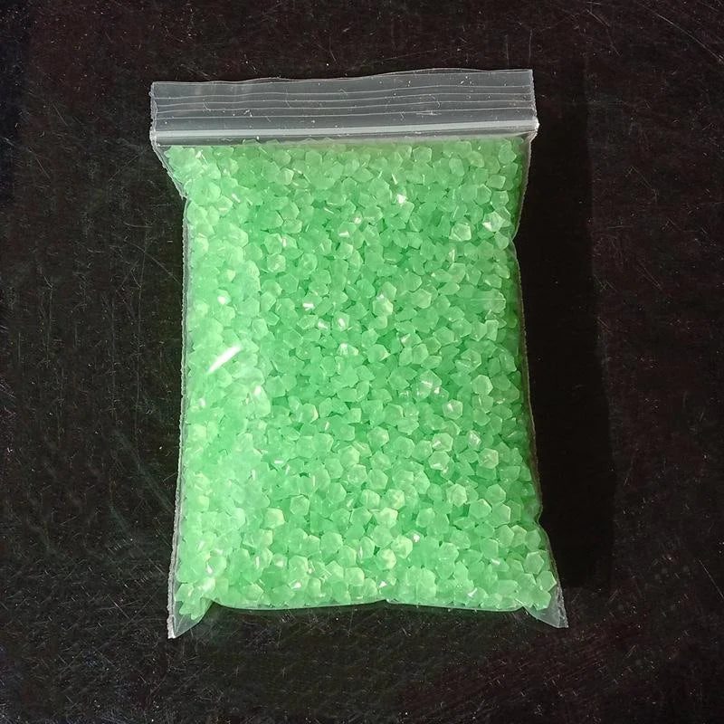 A clear plastic bag filled with bright green glow-in-the-dark decorative pebbles.