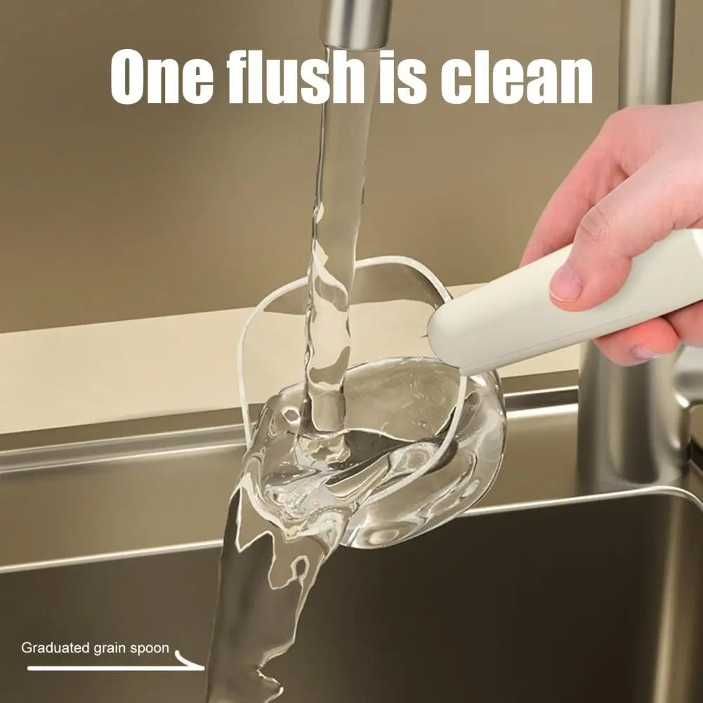 A hand is using a white measuring scoop to flush food down a sink drain, demonstrating that one flush is clean.