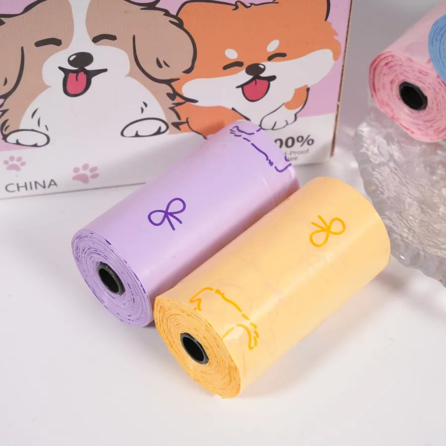 Three rolls of thick dog waste bags in purple and yellow mixed sweet patterns next to a cardboard box featuring dog illustrat