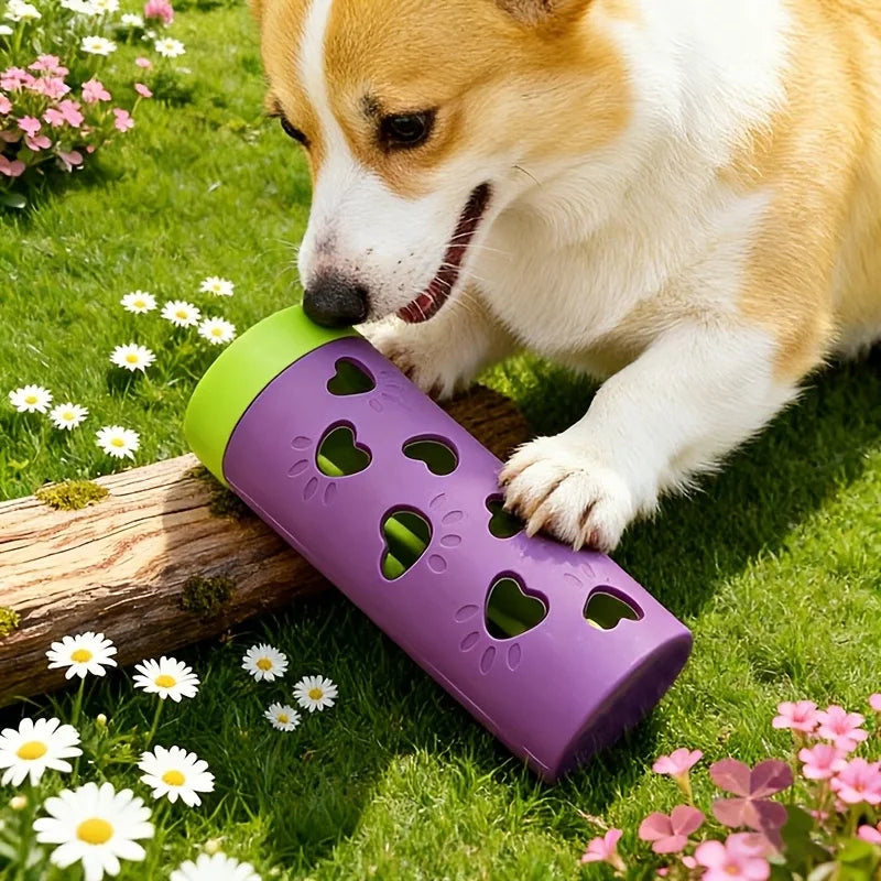 A dog is interacting with a purple, heart-shaped slow feeder treat dispenser in a grassy outdoor setting.