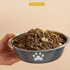 A hand holds a gray stainless steel pet food bowl filled with dry brown pet food.
