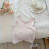 A light pink knitted mini vest with lace trim is displayed on a white surface next to roses and a bow.