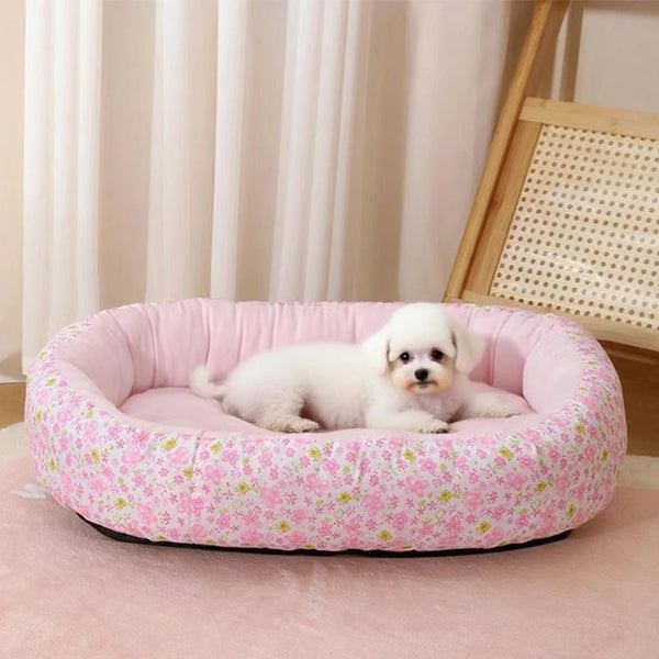 A pink floral pet bed for a small white dog resting on a pink rug.