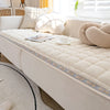 A cozy beige fleece pet bed mat is placed on a light-colored sofa with decorative pillows.