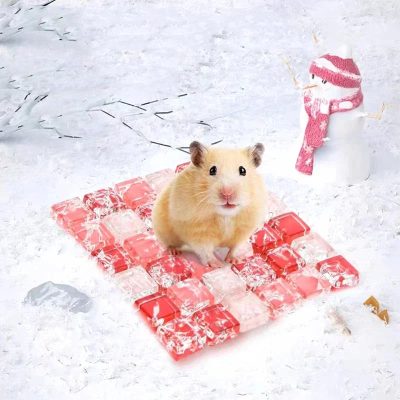 A fluffy brown hamster is sitting on a red cooling mat with a pink knitted snowman decoration.