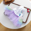 A white and purple tulle birthday suit for a small puppy is displayed on a wooden tray.