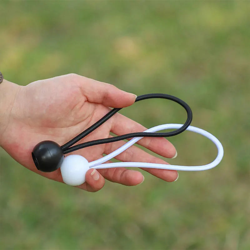 A hand holds a black and white bungee ball set with cords for outdoor use.