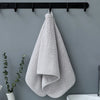A folded light gray plush microfiber bath towel hanging on a black rack against a gray wall.